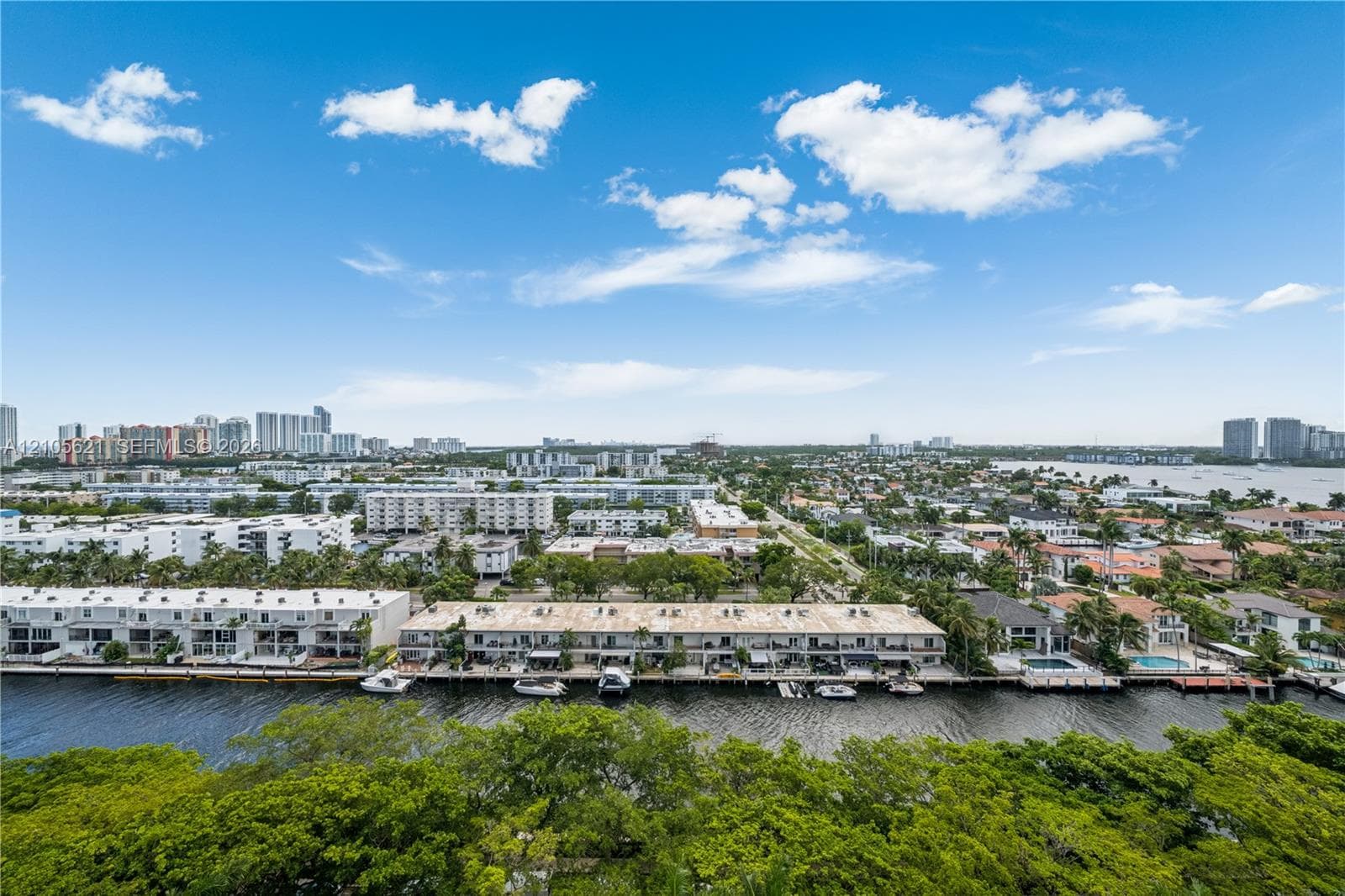 Aerial perspective featuring a waterfront bulkhead, private boat slips, multi-level residential structures, and an expansive urban cityscape