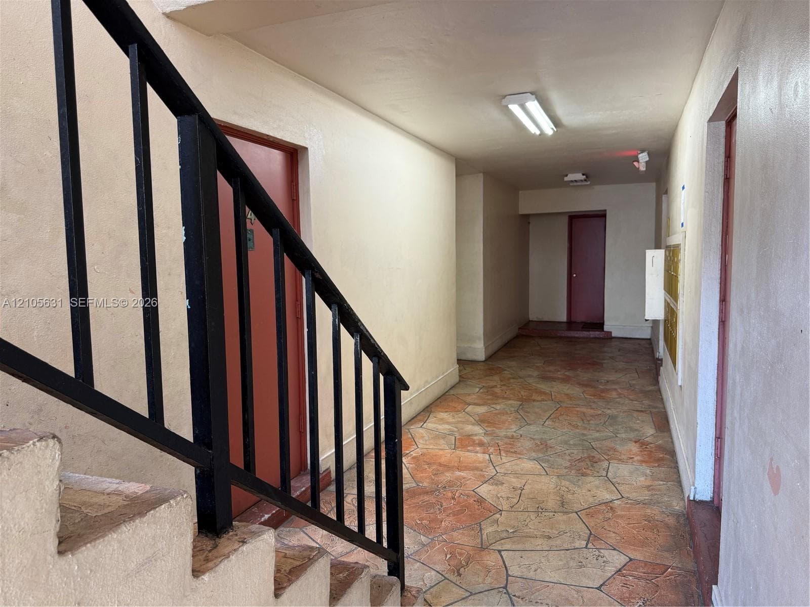 Interior corridor featuring stone-patterned tile flooring, black metal handrails, and built-in mail receptacles