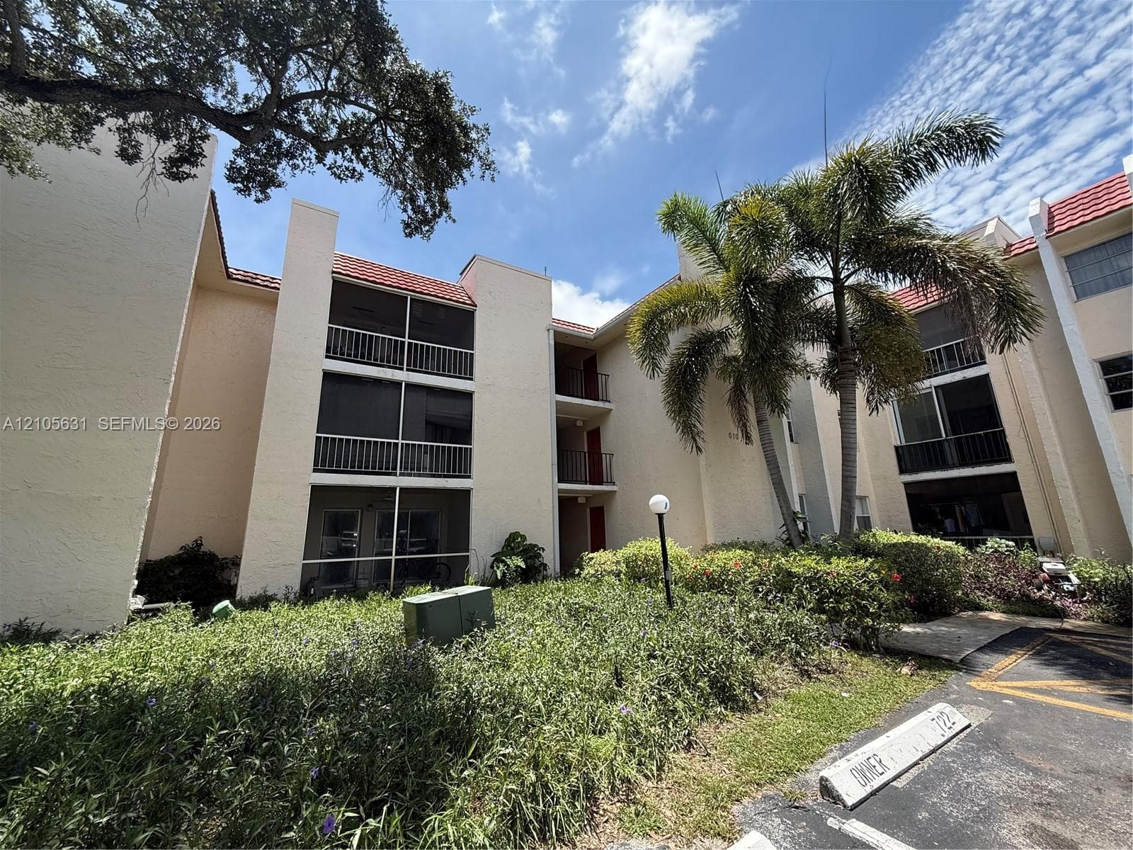 Multi-story stucco exterior featuring screened balconies, red tile roofing, and mature palm tree landscaping