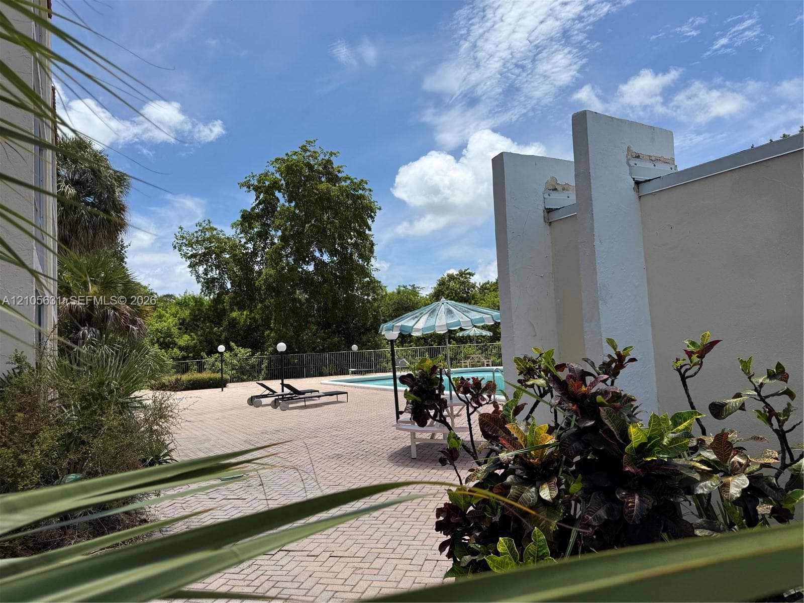 Outdoor pool area featuring a paved deck, perimeter fencing, and mature landscaping