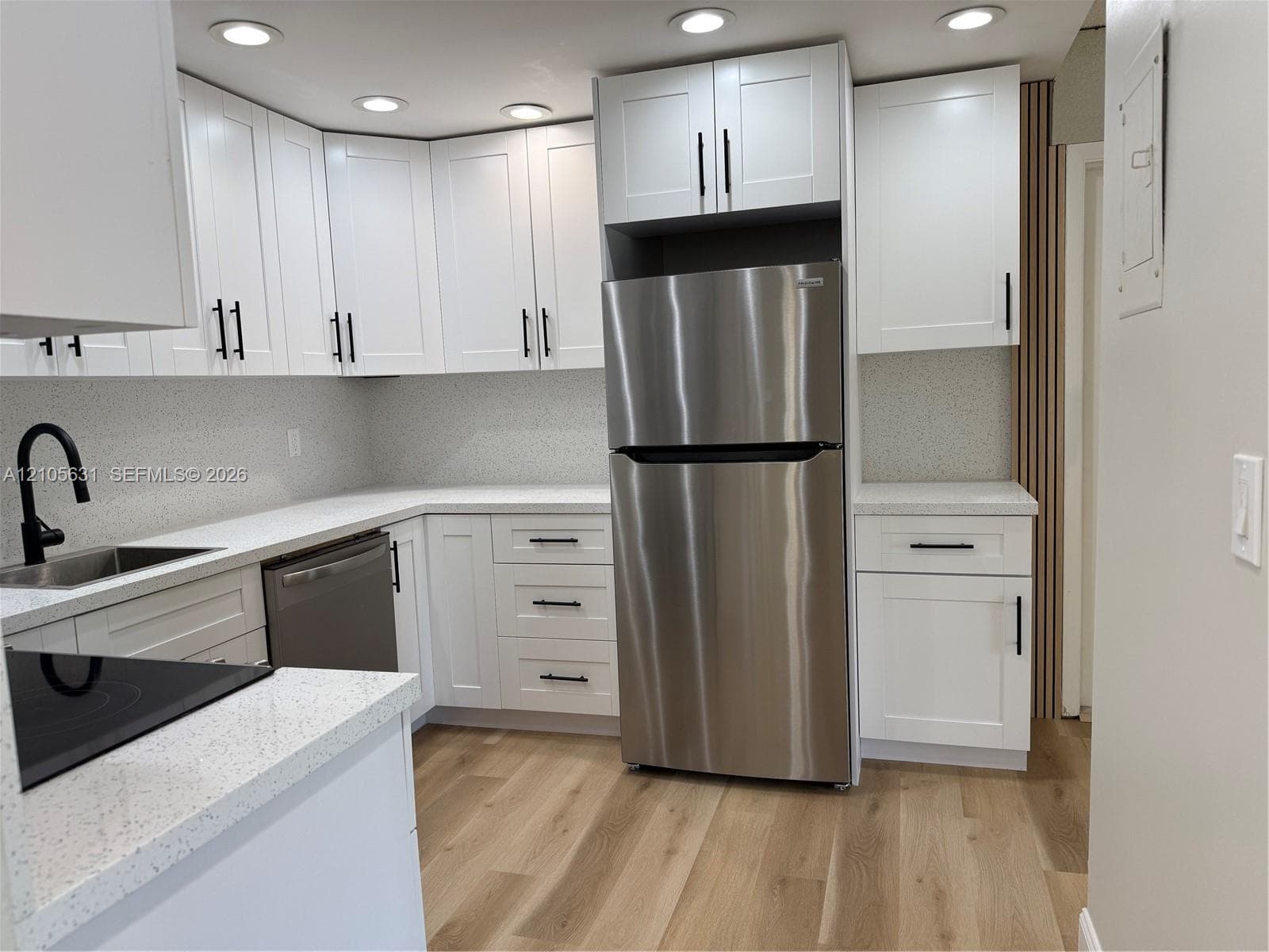 Kitchen featuring white shaker-style cabinetry, quartz countertops, stainless steel appliances, matte black hardware, and wood-finish flooring