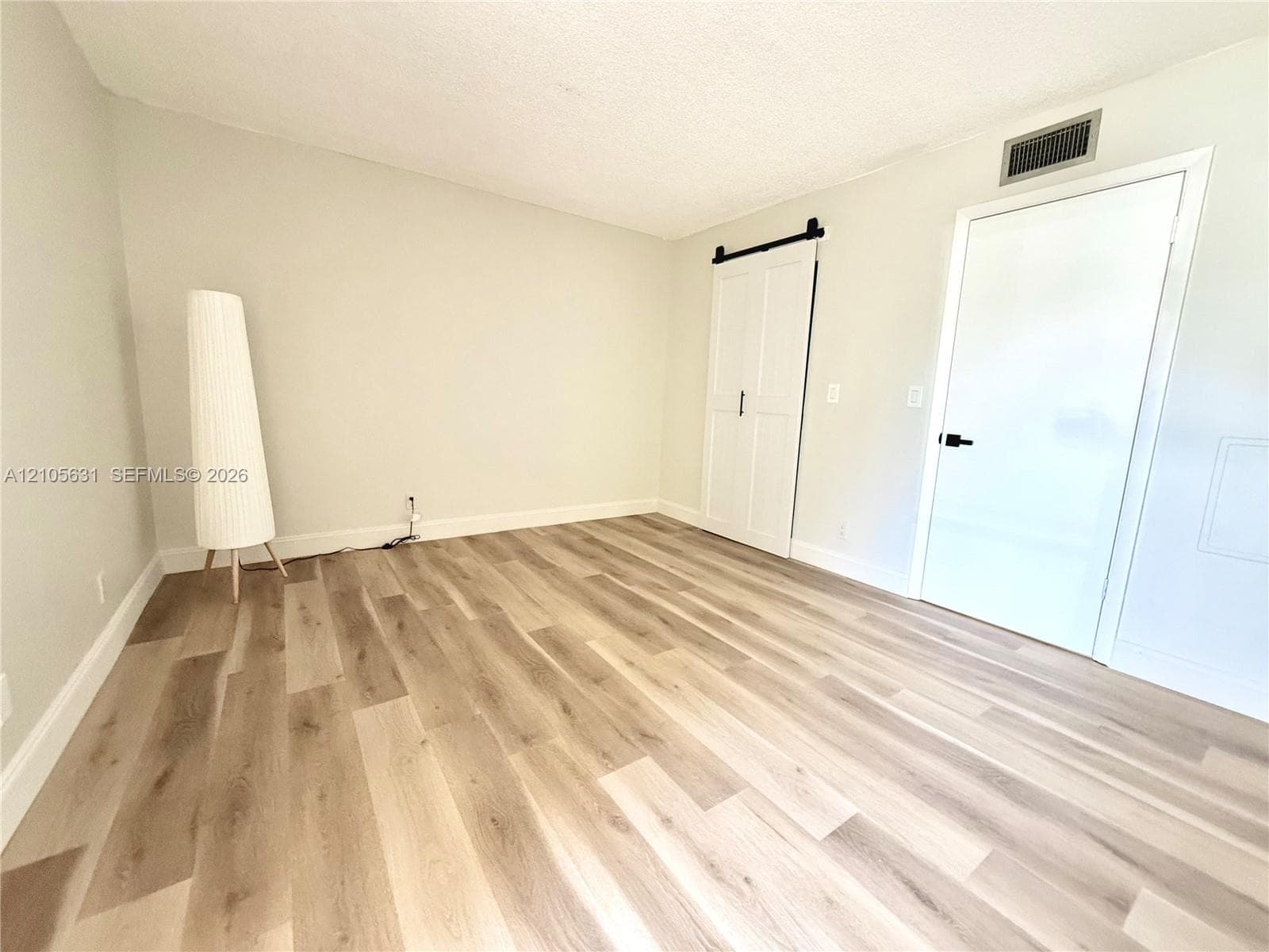 Room featuring wood-finish flooring, white double sliding barn door with matte black hardware, and a solid-panel door with a matte black lever handle
