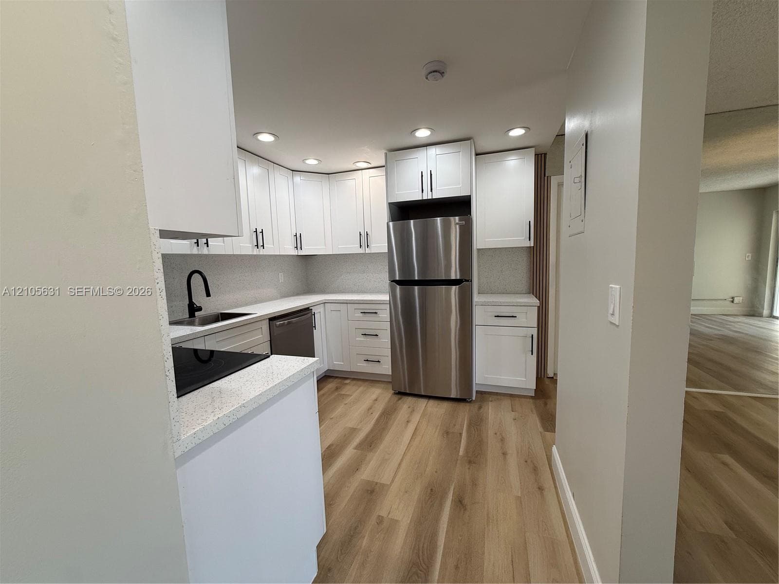 Kitchen featuring white Shaker-style cabinetry, stainless steel appliances, light-toned stone-finish countertops, matte black plumbing fixtures, and wood-finish flooring