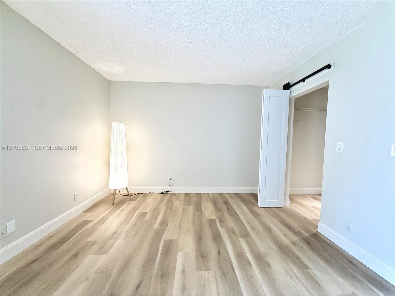 Neutral interior space featuring wood-finish flooring, light-toned walls, and a white interior door on a black sliding track