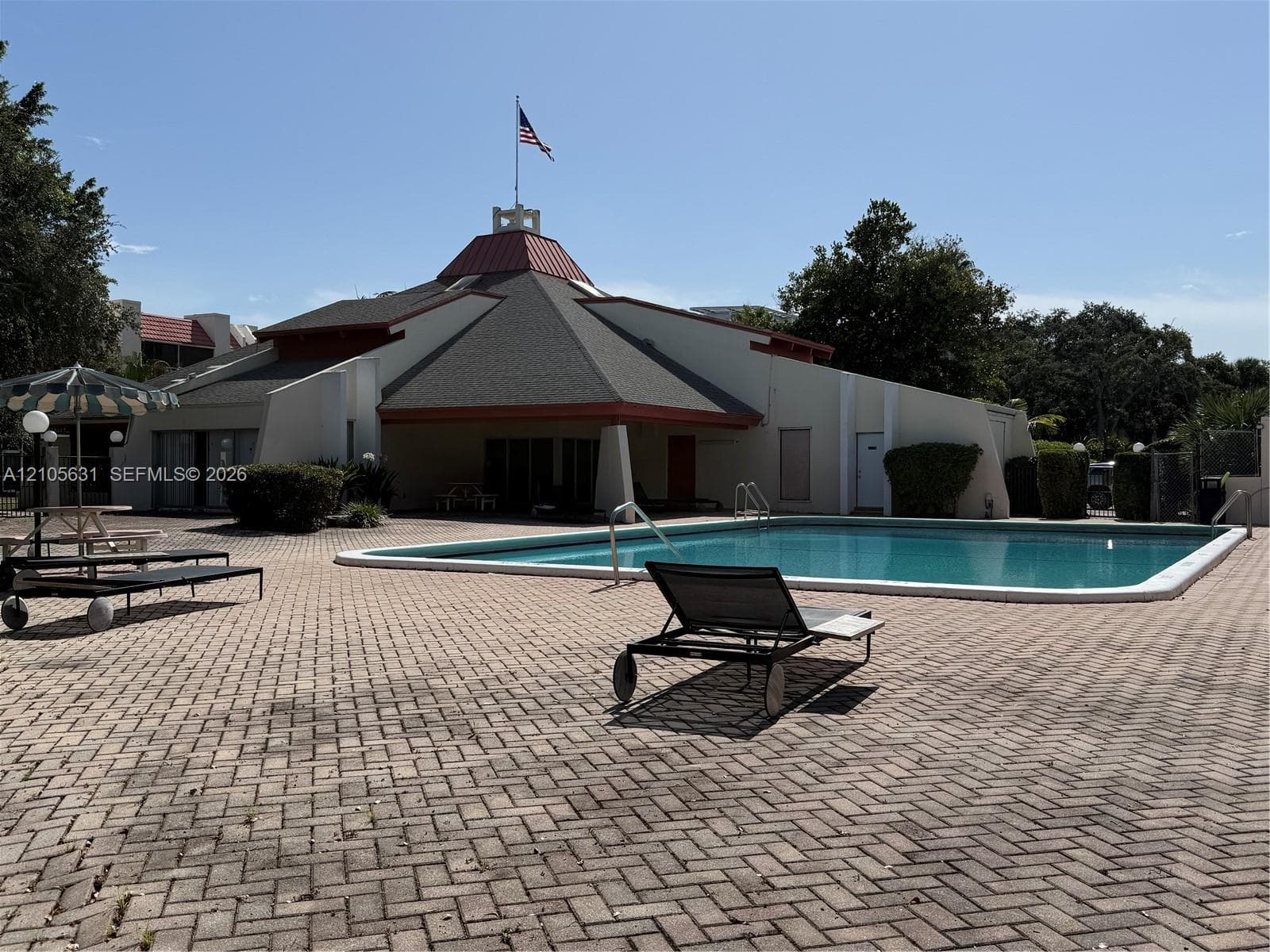 In-ground swimming pool with surrounding paver deck, featuring a multi-faceted roof structure and a central decorative cupola