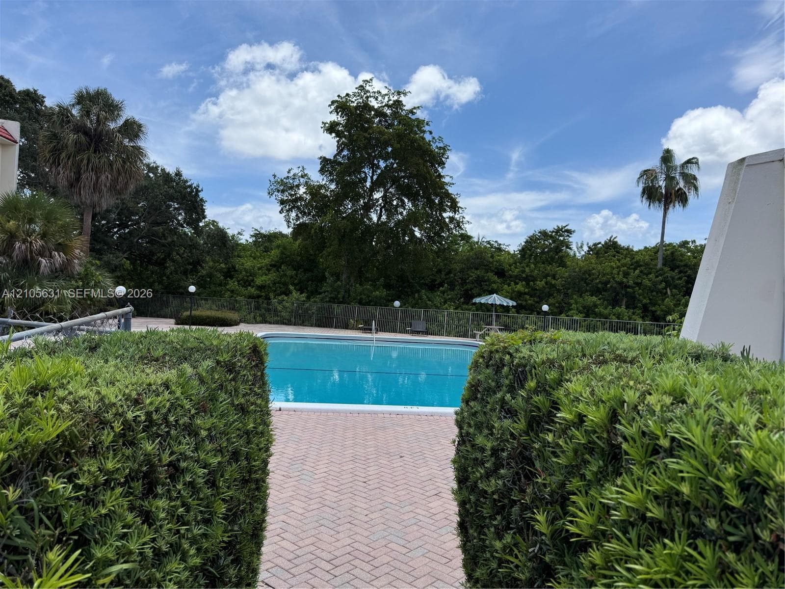 Outdoor swimming pool featuring a brick paver deck, perimeter fencing, and mature shrubbery