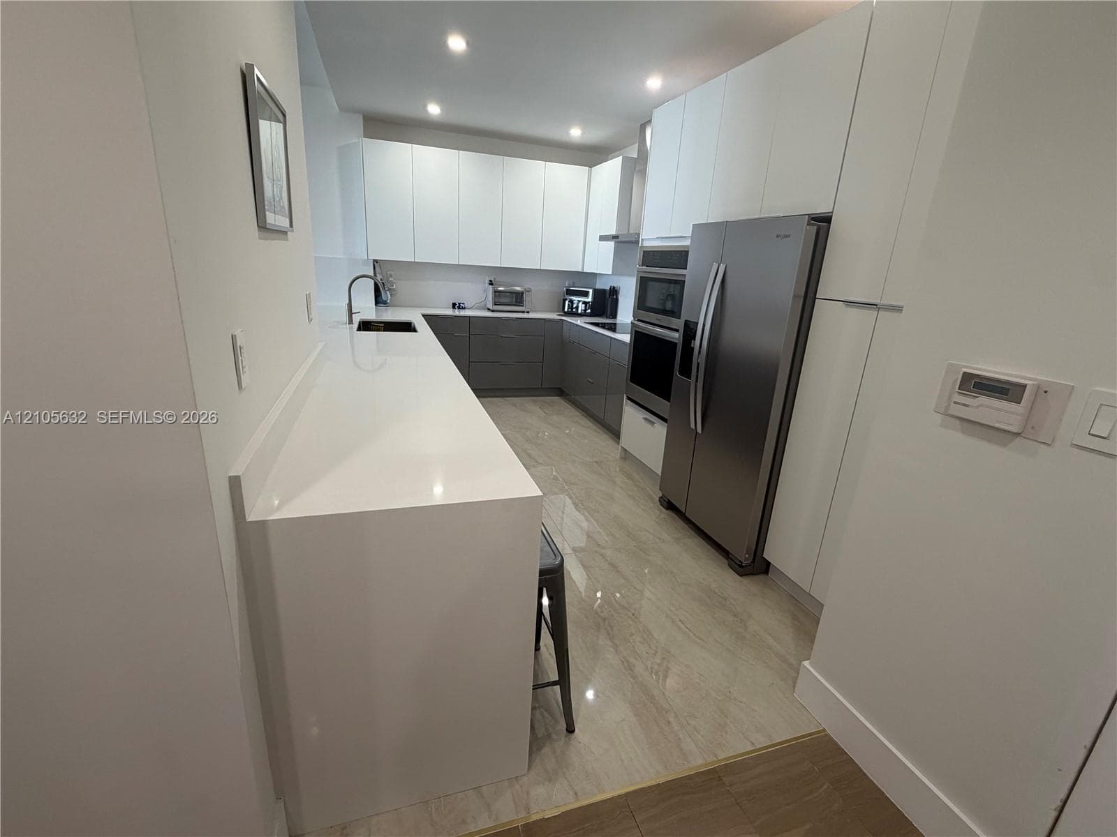 Kitchen featuring a waterfall-edge quartz countertop, two-tone flat-panel cabinetry, stainless steel built-in oven and microwave, stainless steel refrigerator, and polished stone-finish flooring