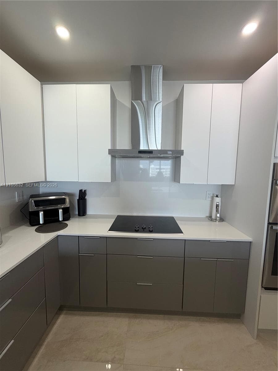 Kitchen featuring two-tone cabinetry, white countertops, a smooth-surface cooktop, a stainless steel chimney-style range hood, and recessed ceiling lighting