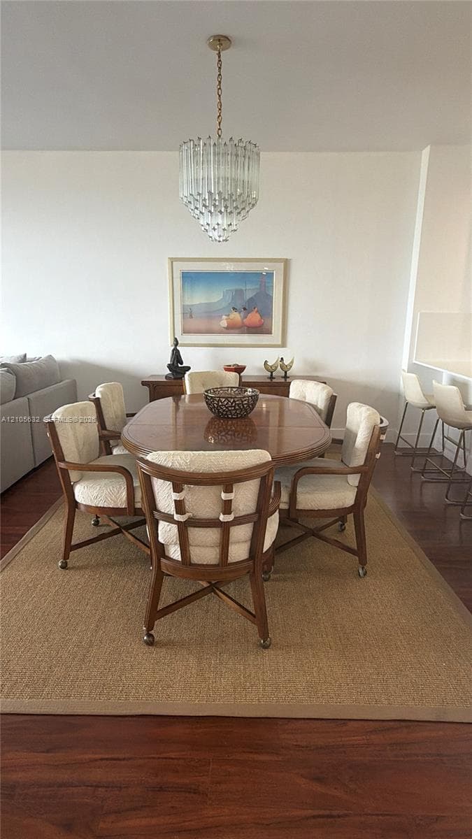 Dining area featuring dark wood-finish flooring, a tiered crystal chandelier, and a built-in kitchen breakfast bar