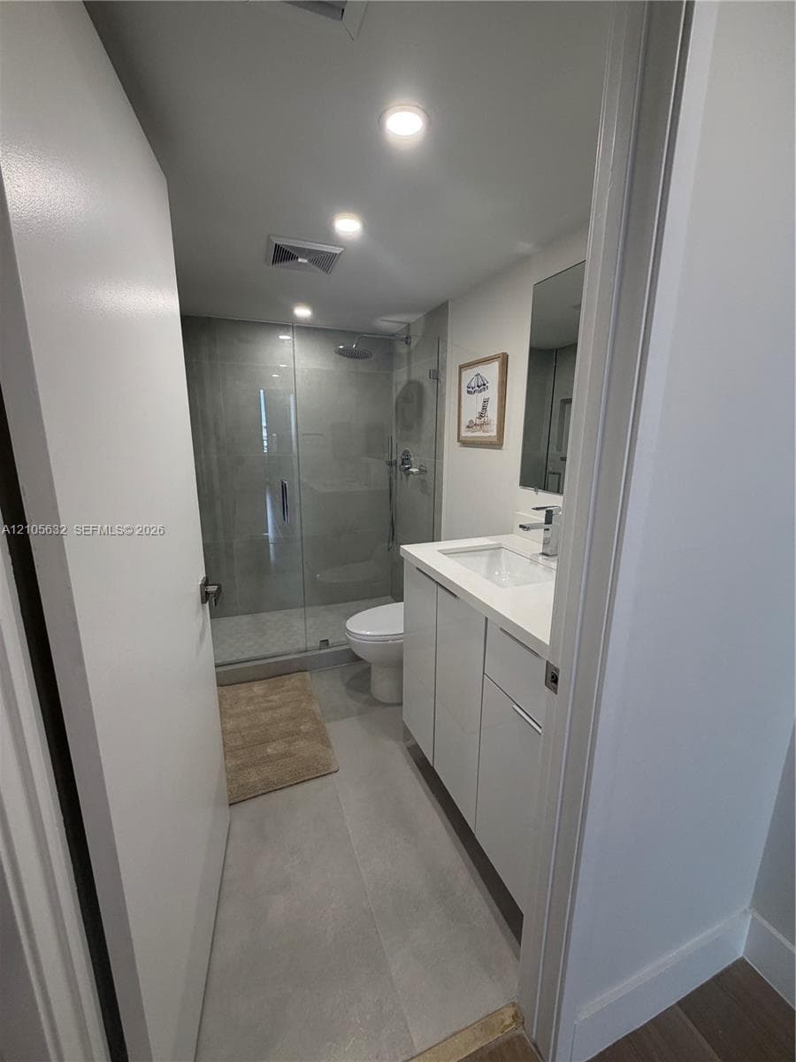 Bathroom featuring a white vanity with a rectangular sink, quartz countertop, glass-enclosed shower, and recessed ceiling lighting