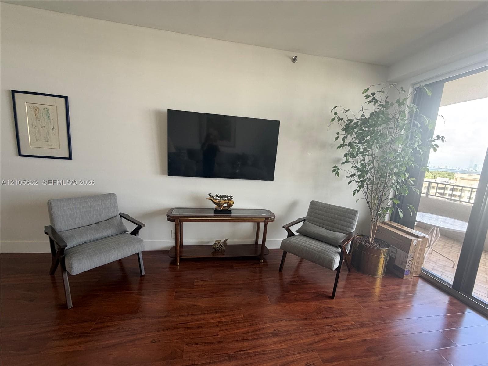 Living area featuring wood-finish flooring and a wall-mounted flat-panel television, with glass sliding doors providing external access