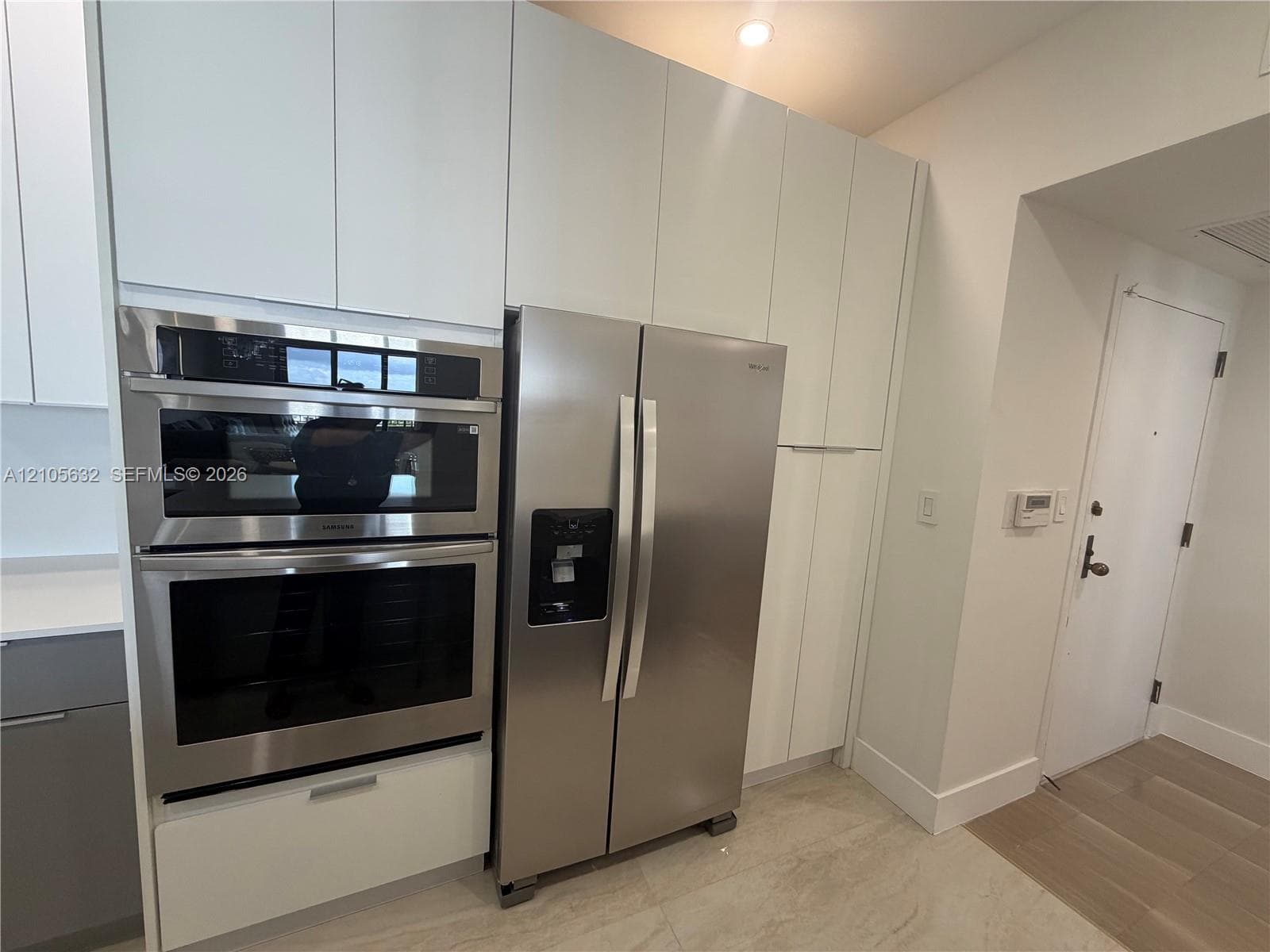 Kitchen featuring white floor-to-ceiling cabinetry, stainless steel side-by-side refrigerator, built-in double oven, and light-toned tile flooring