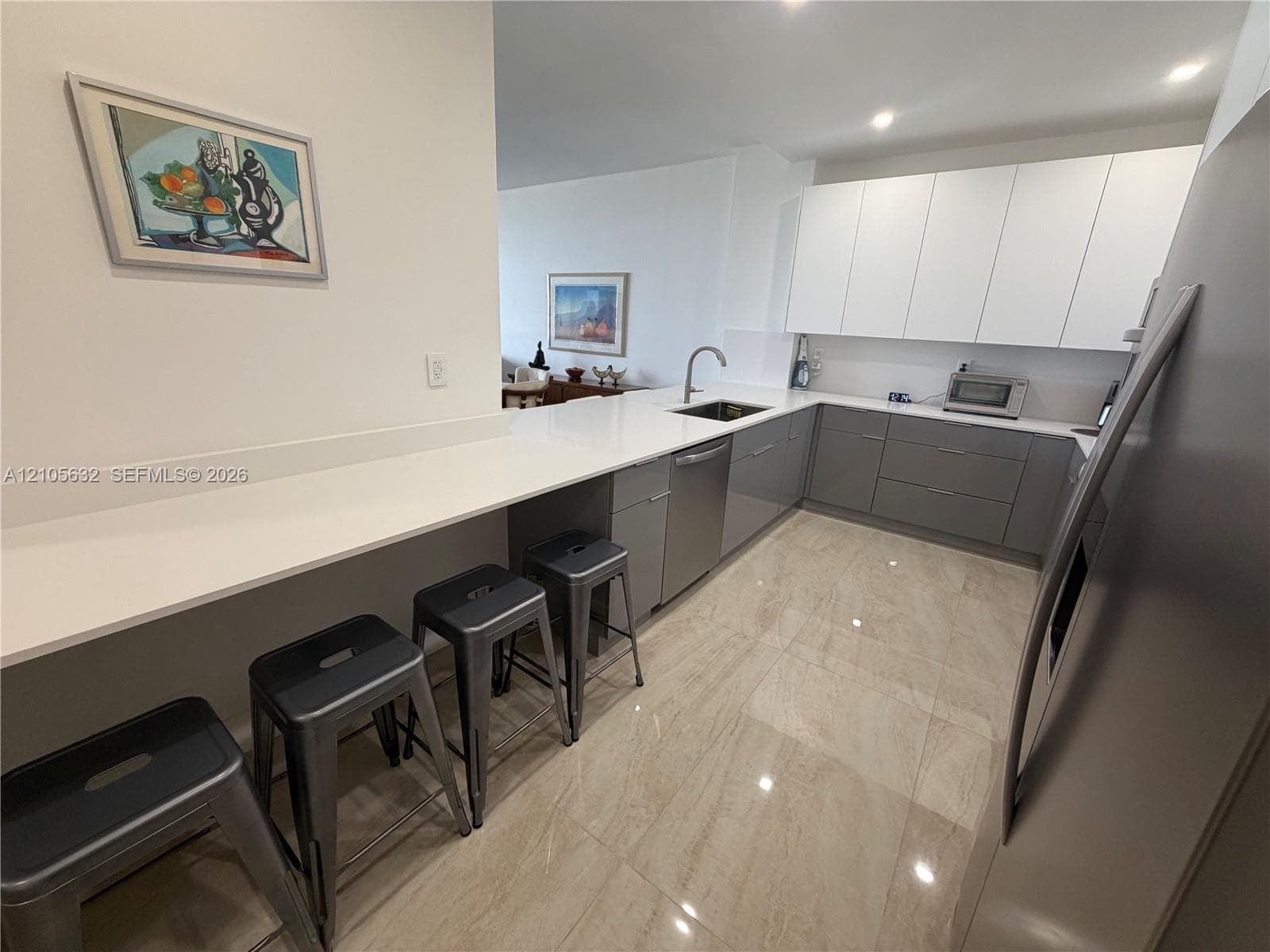 Kitchen featuring white and grey high-gloss cabinetry, stone-surface countertops, recessed lighting, stainless steel appliances, and large-format neutral-toned tile flooring