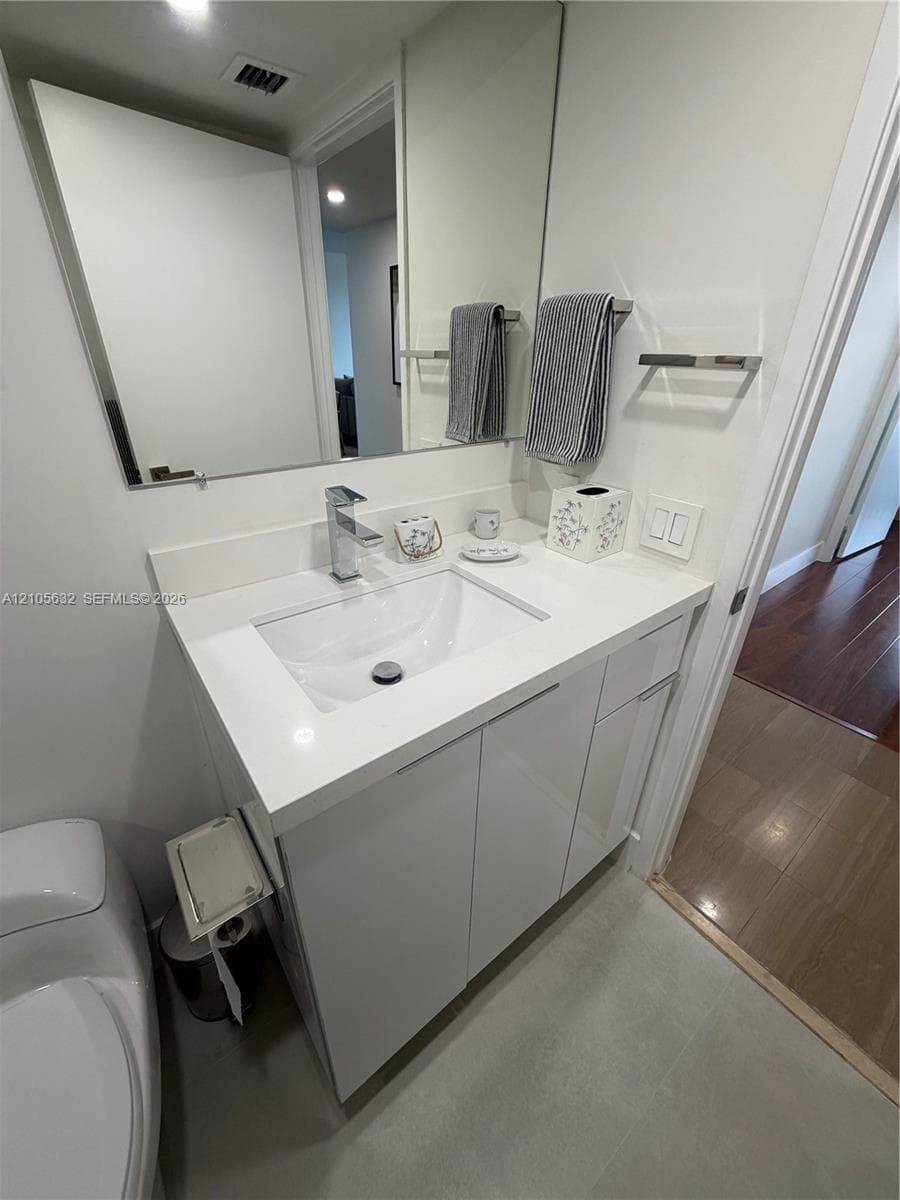 Modern vanity with white cabinetry, solid-surface countertop, rectangular undermount sink, chrome faucet, and expansive wall-mounted mirror