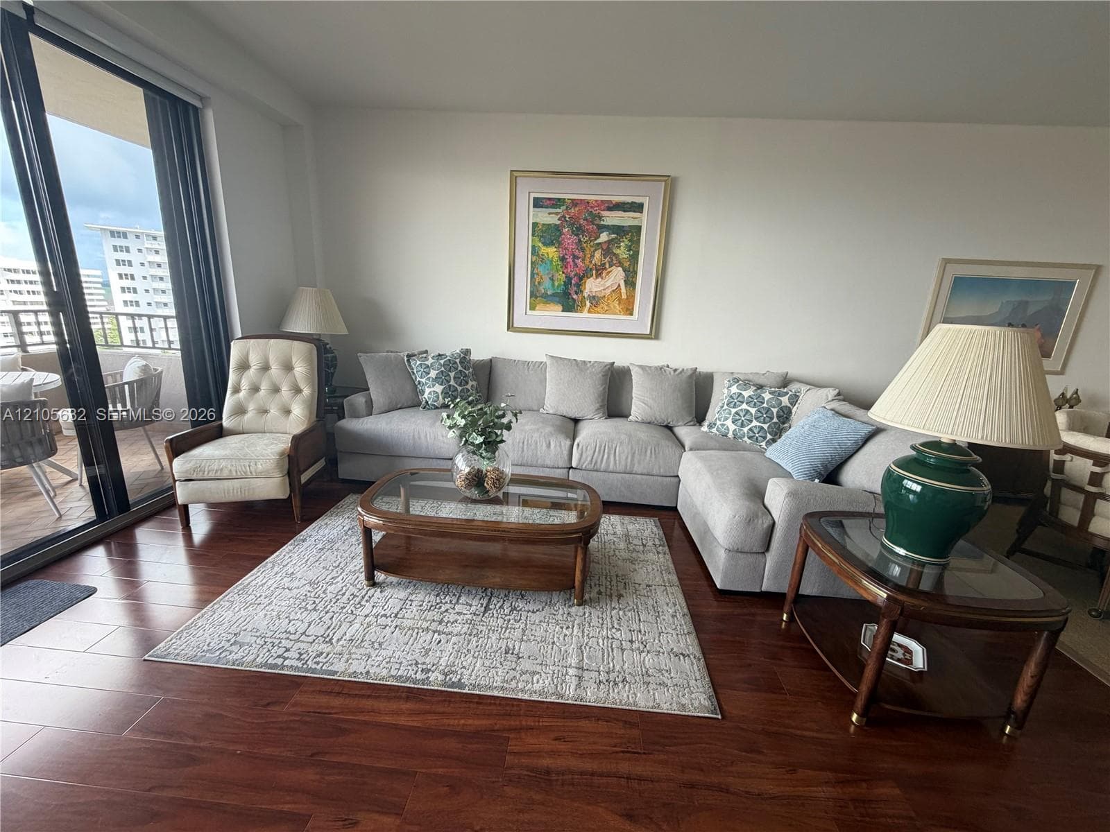Living area featuring dark wood-finish flooring and floor-to-ceiling sliding glass doors opening to a covered balcony