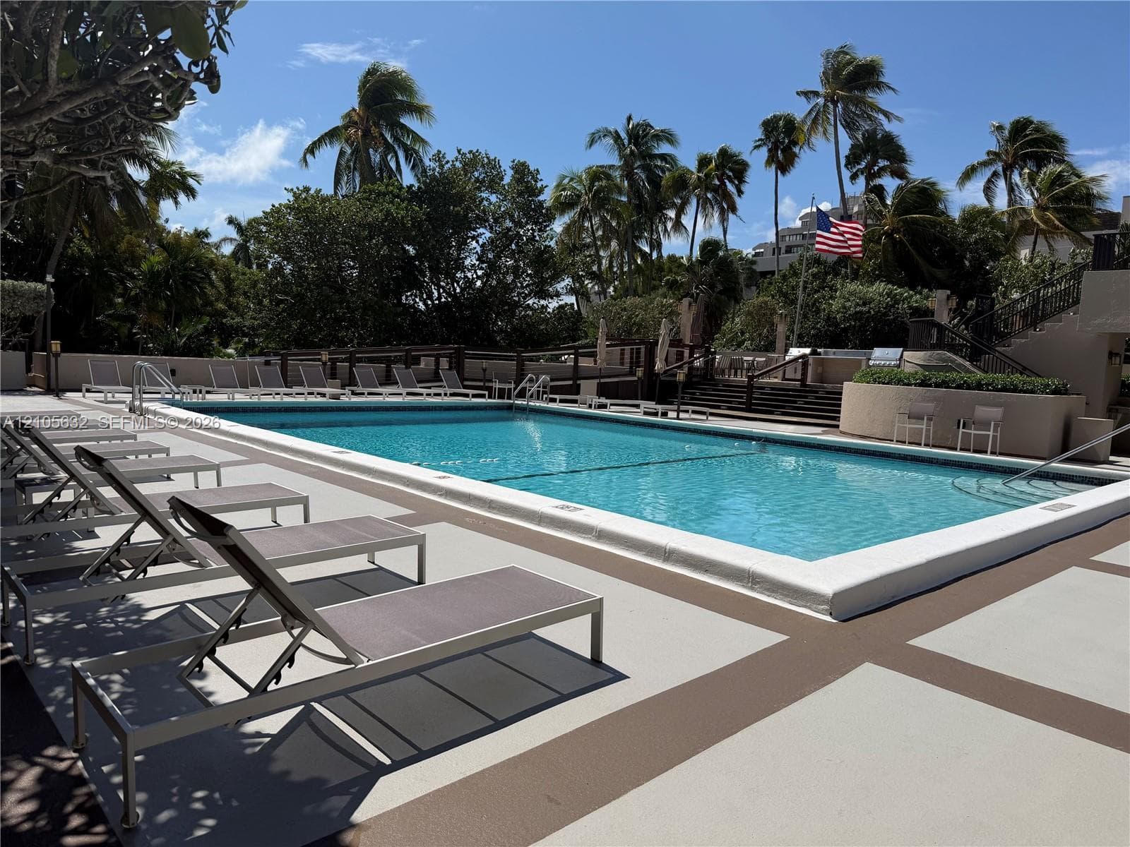 Swimming pool with concrete decking, perimeter fencing, mature palm trees, and tiered landscaping