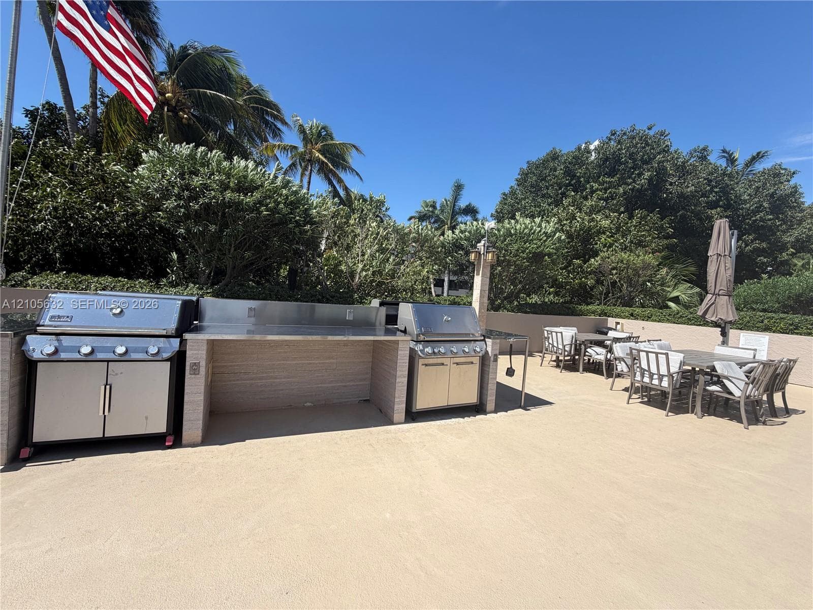 Outdoor kitchen featuring dual stainless steel grills, a stone-finish preparation counter, and a spacious paved patio area