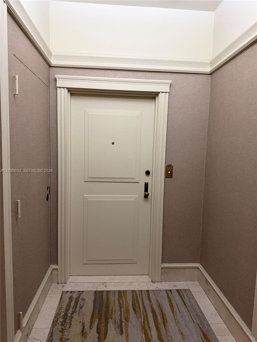 Entryway featuring a two-panel door, fluted door casing, crown molding, and stone flooring