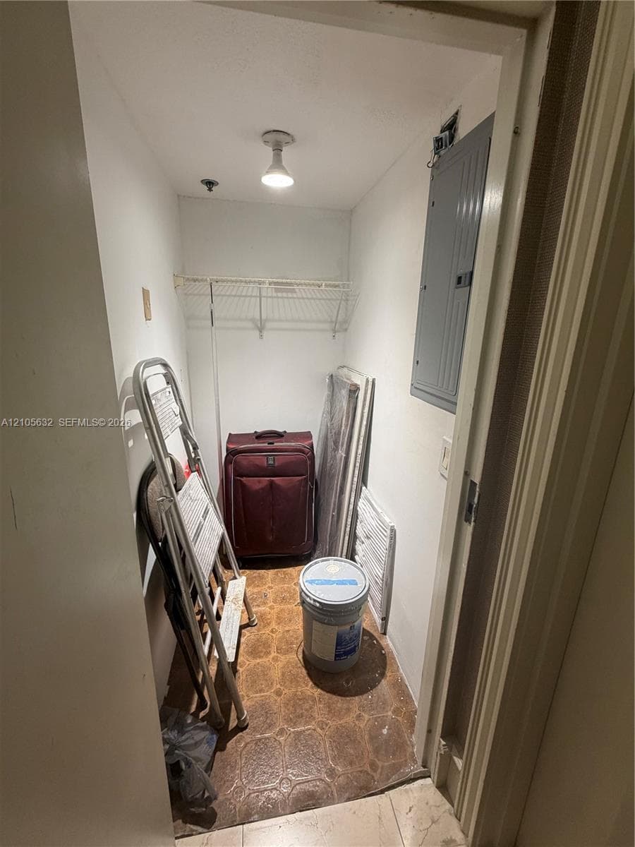 Utility closet featuring a ceiling-mounted light fixture, wall-mounted electrical panel, and built-in wire shelving