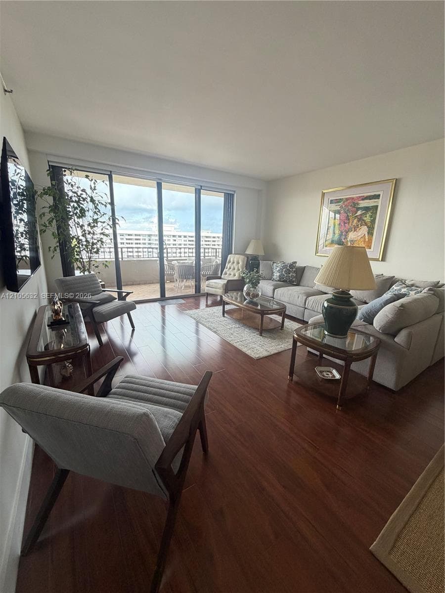 Living area featuring dark wood-finish flooring, floor-to-ceiling glass sliding doors, and a private balcony