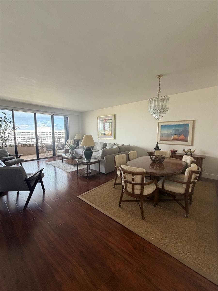 Open-concept living space featuring wood-finish flooring, floor-to-ceiling sliding glass doors, a decorative crystal chandelier, and a private balcony