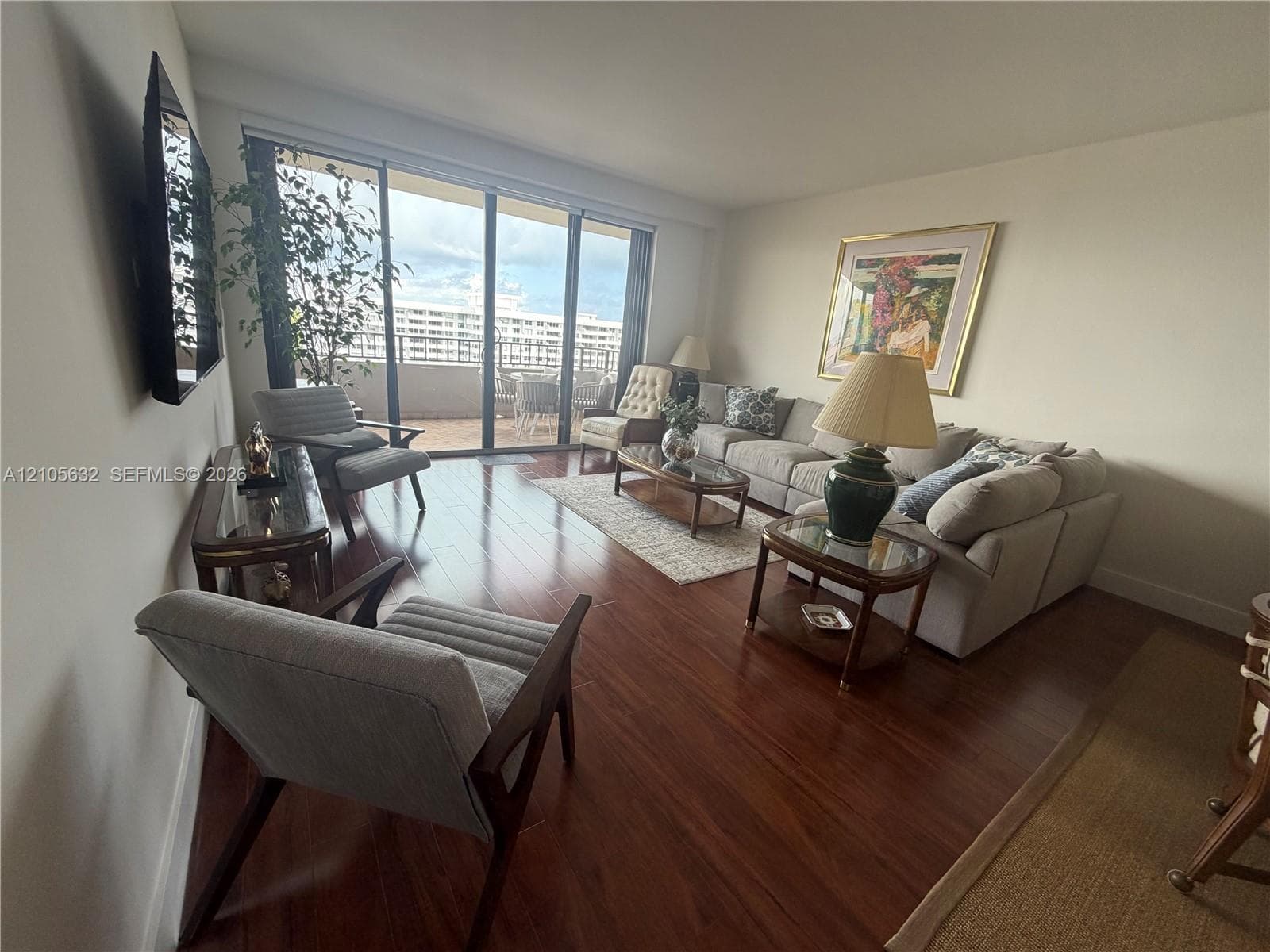Living area featuring dark wood-finish flooring and floor-to-ceiling sliding glass doors opening to a private balcony
