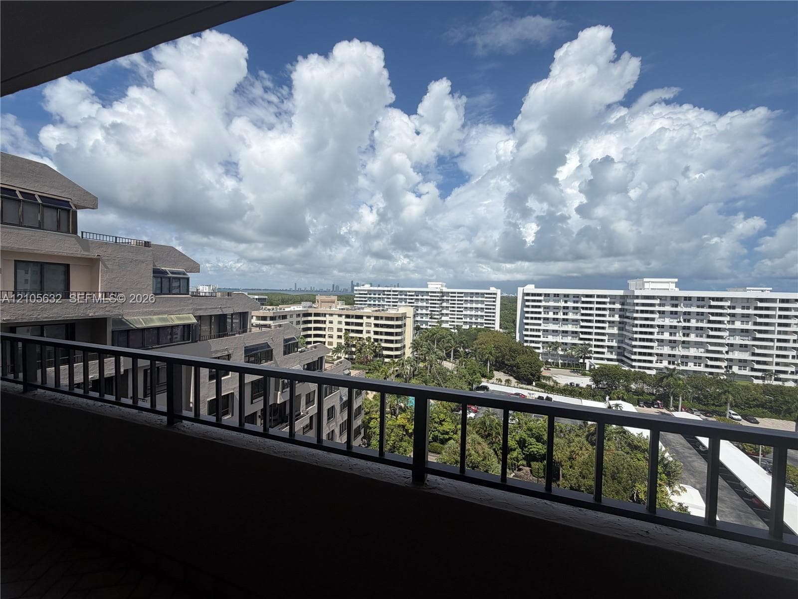 Covered balcony with a black metal railing and concrete flooring overlooking the surrounding cityscape