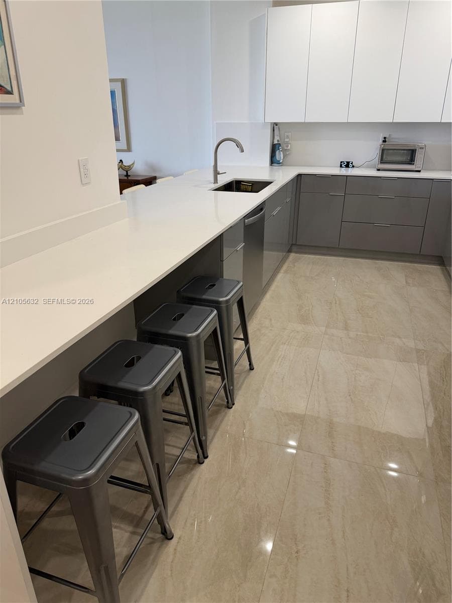 Kitchen featuring high-gloss slab cabinetry, expansive stone-surface countertops, polished tile flooring, and a stainless steel undermount sink with a gooseneck faucet