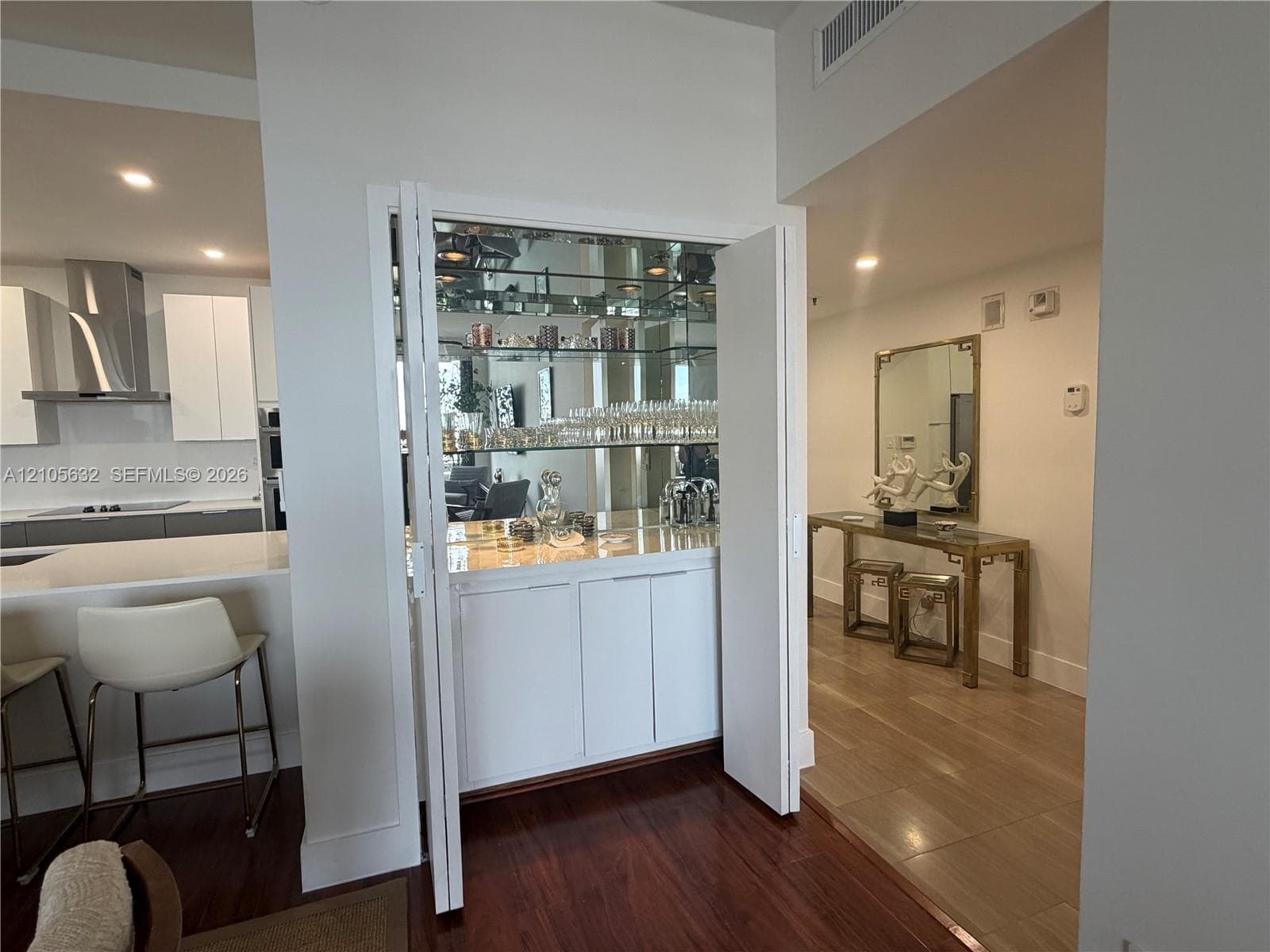 Built-in wet bar featuring mirrored shelving, recessed lighting, stone countertop, and custom cabinetry