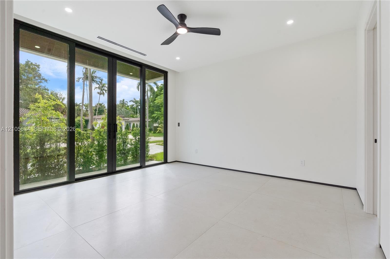 Large-format tile flooring, multi-panel sliding glass doors with dark frames, matte black ceiling fan, and recessed lighting
