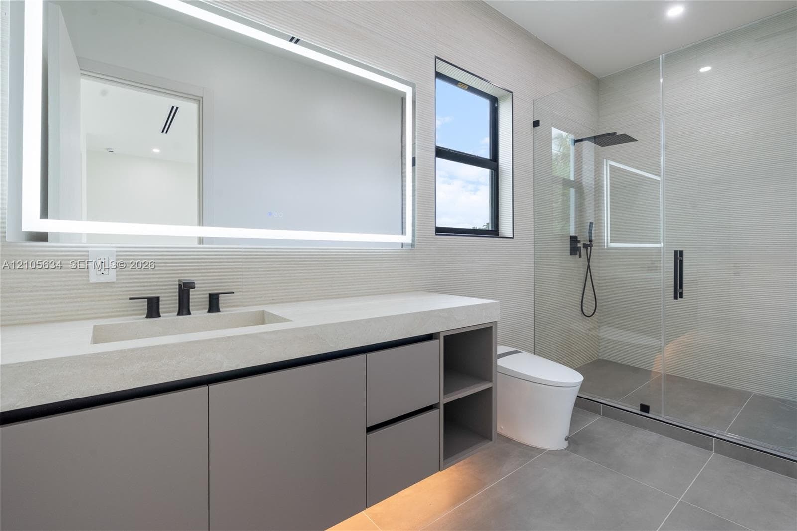 Floating vanity with integrated sink, stone-finish countertop, under-cabinet lighting, LED-backlit mirror, and glass-enclosed walk-in shower with matte black rainfall fixture