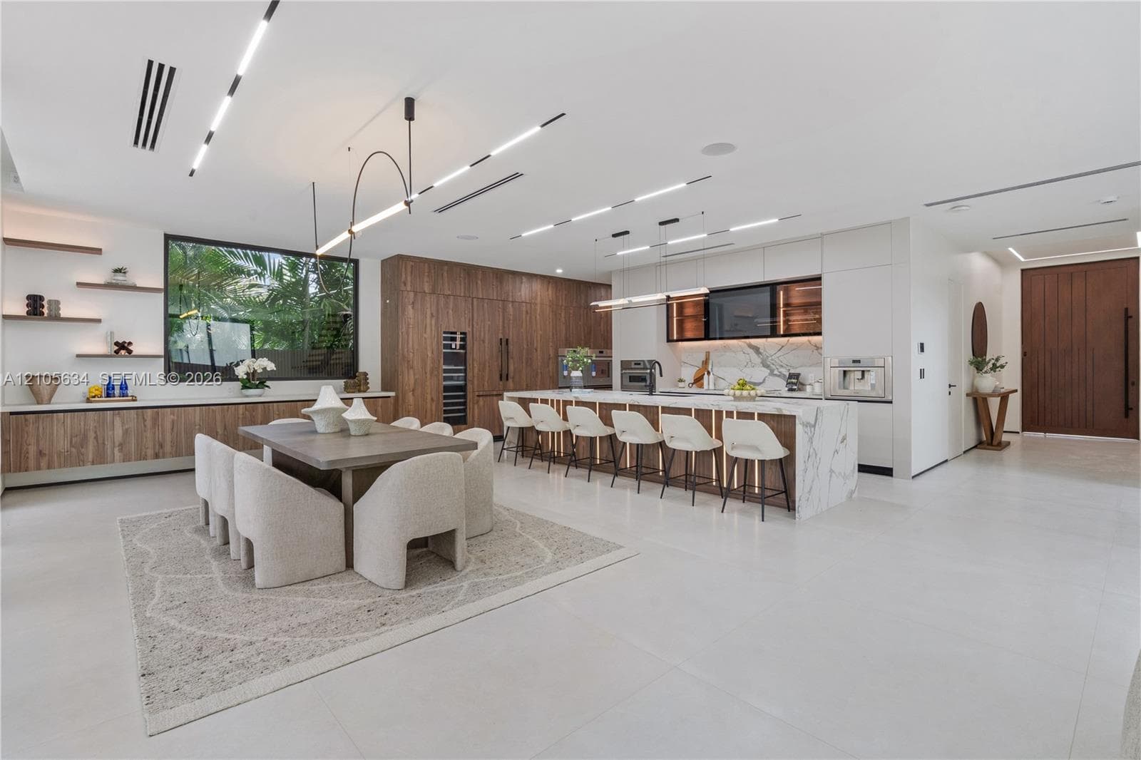 Open-concept kitchen featuring a waterfall-edge stone island, built-in panel-ready appliances, wood-finish cabinetry, linear recessed ceiling lighting, and porcelain tile flooring