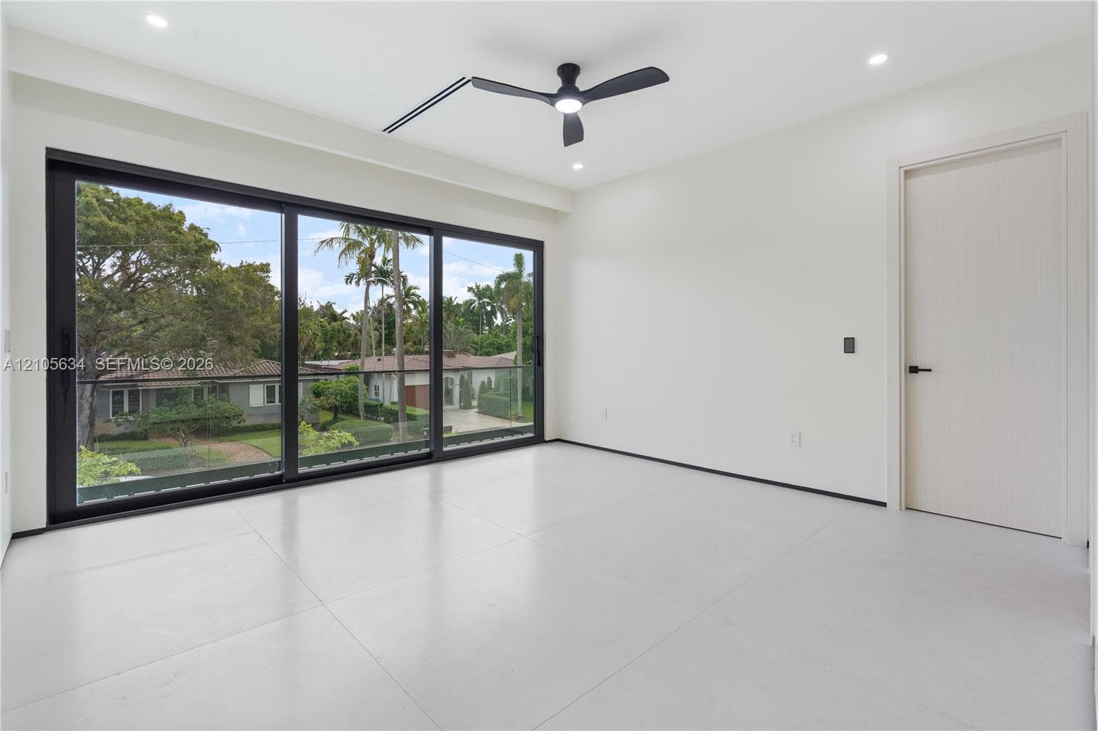 Floor-to-ceiling sliding glass doors with black frames, large-format tile flooring, recessed lighting, matte black ceiling fan, and solid-core interior door