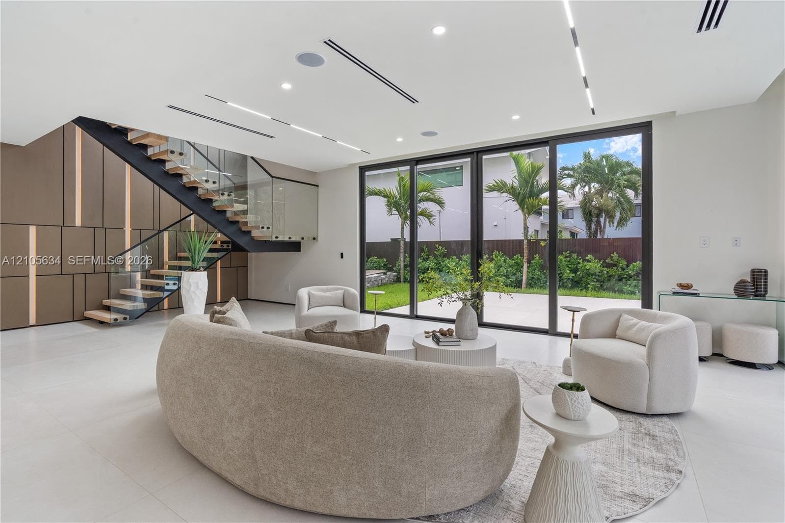 Open-concept interior featuring large-format tile flooring, a custom metal staircase with a glass railing, built-in decorative wall paneling, and floor-to-ceiling sliding glass doors