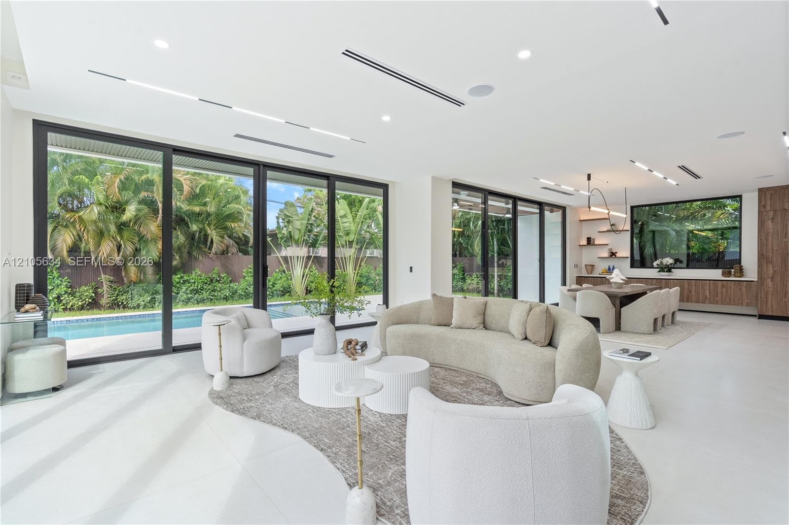 Open-concept interior featuring large-format flooring, expansive floor-to-ceiling sliding glass doors, recessed linear lighting, and built-in wood cabinetry