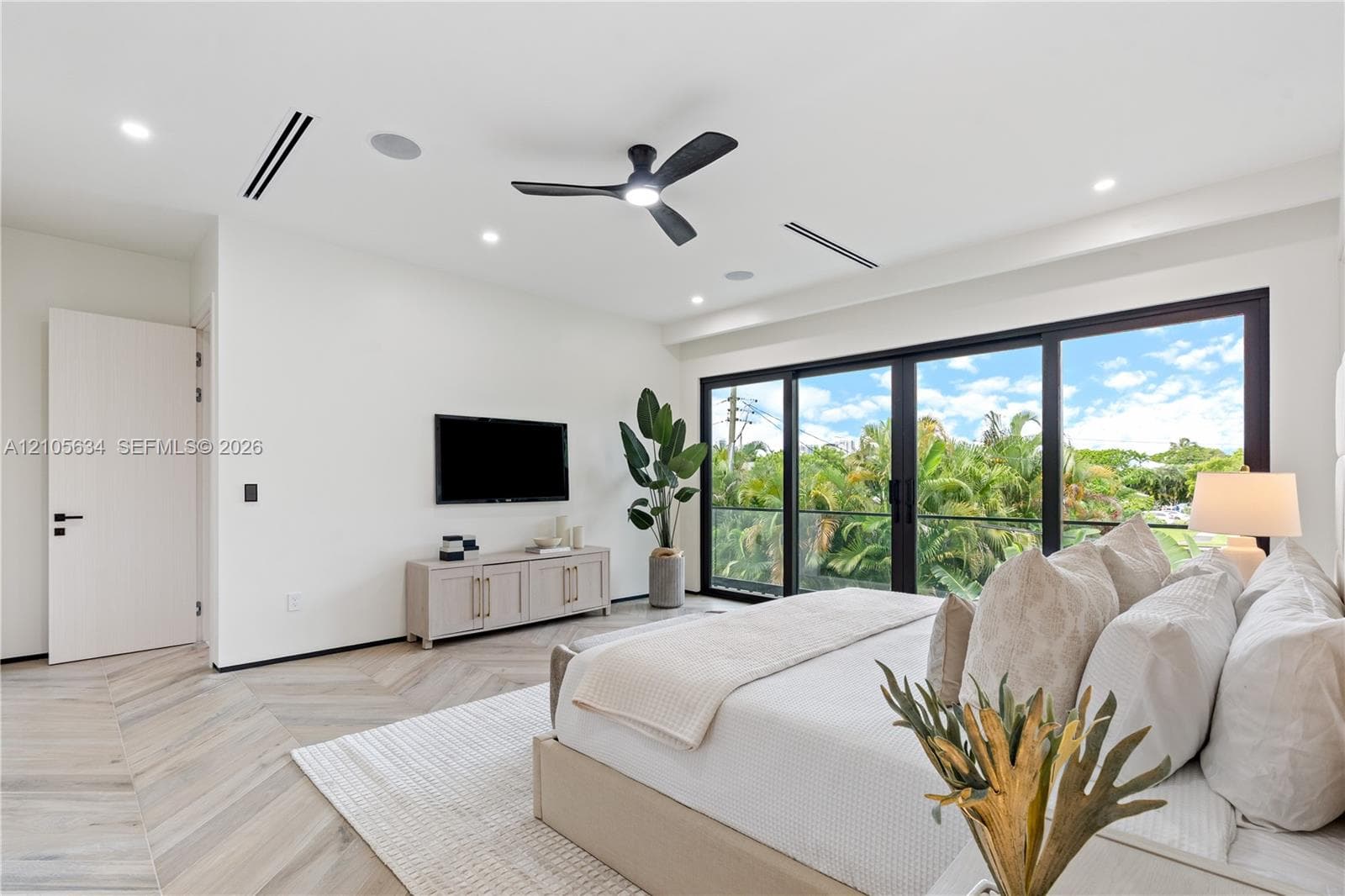 Herringbone-patterned wood-finish flooring, floor-to-ceiling glass sliding doors, recessed lighting, ceiling fan with integrated light, and built-in ceiling speakers