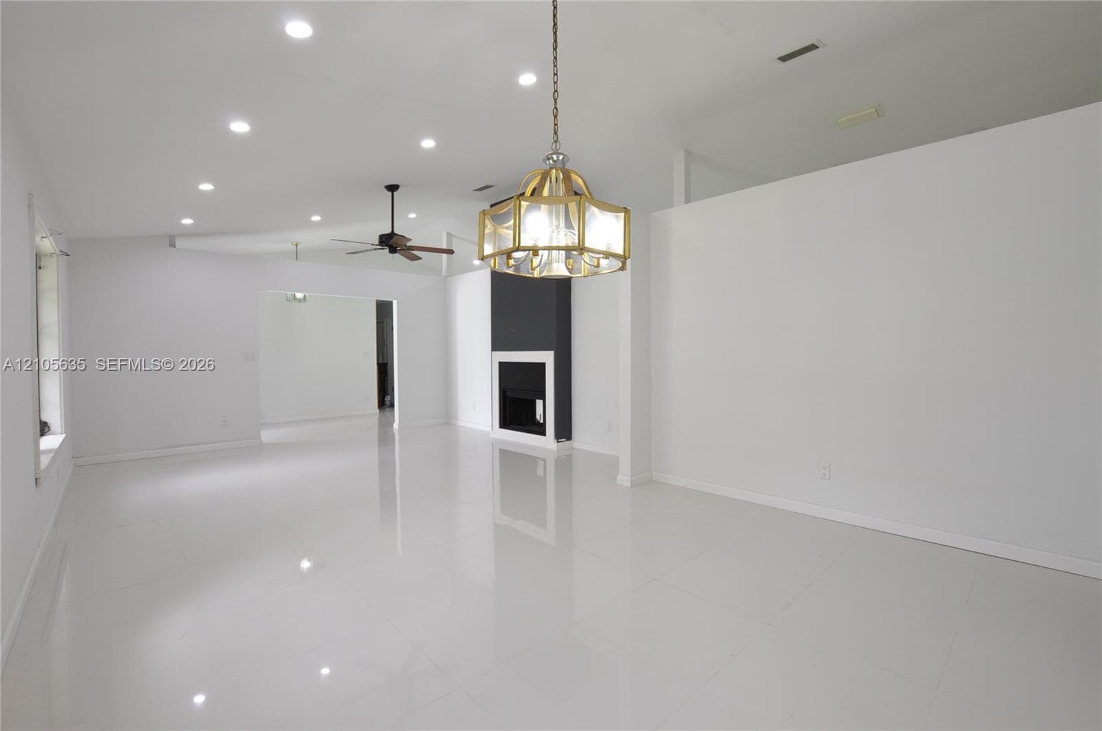 Interior space featuring polished white tile flooring, recessed lighting, a multi-light metallic chandelier, a ceiling fan, and a fireplace with a black surround and white mantel
