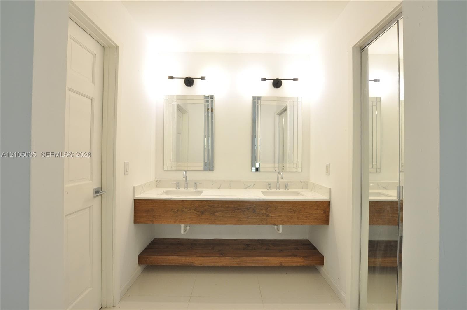 Floating vanity with a wood-finish frame, stone countertop, dual undermount sinks, wall-mounted light fixtures, and rectangular mirrors
