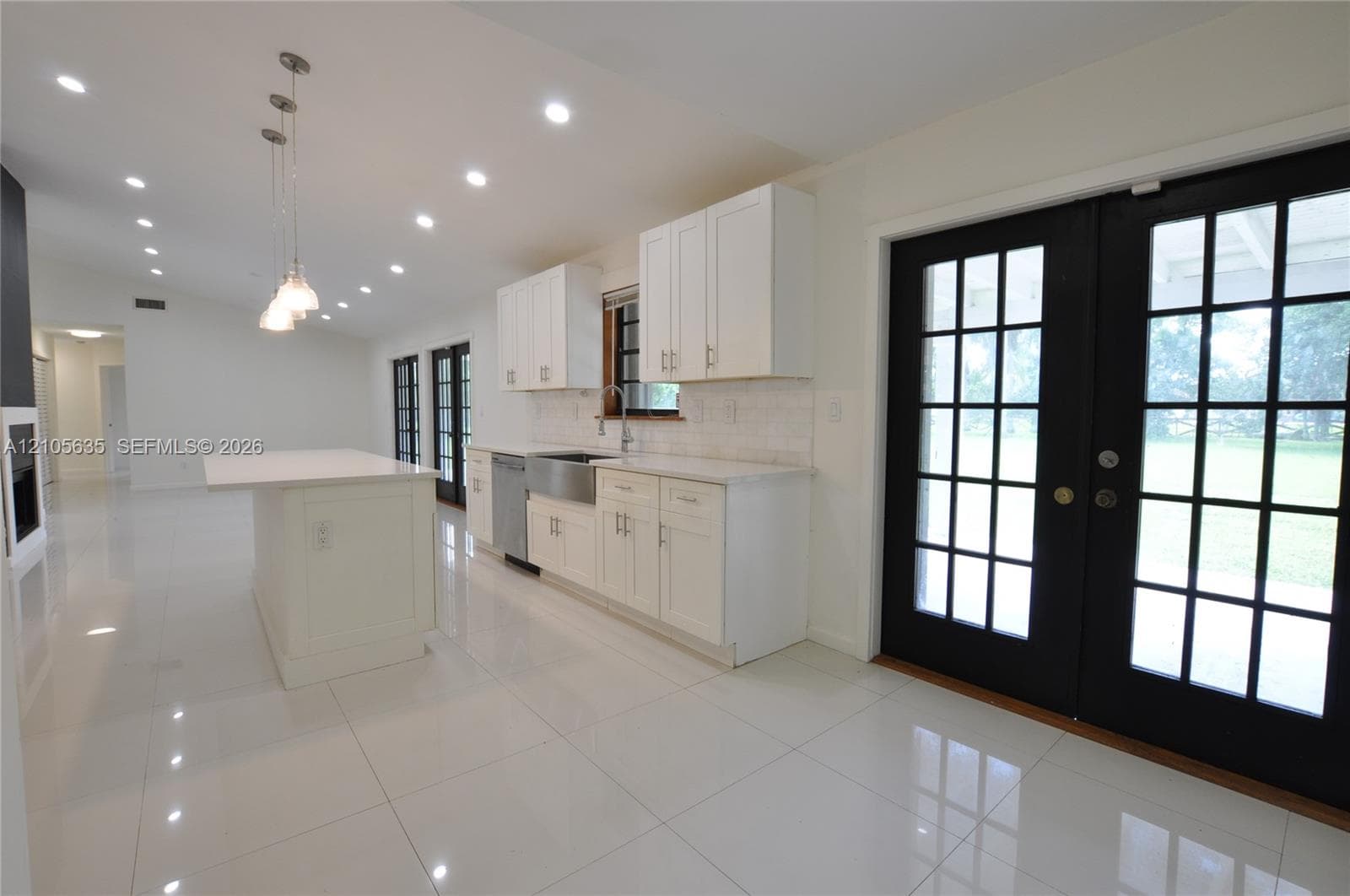 Kitchen featuring white cabinetry, an island with stone-surface countertop, stainless steel farmhouse-style sink, recessed lighting, and black-framed French doors