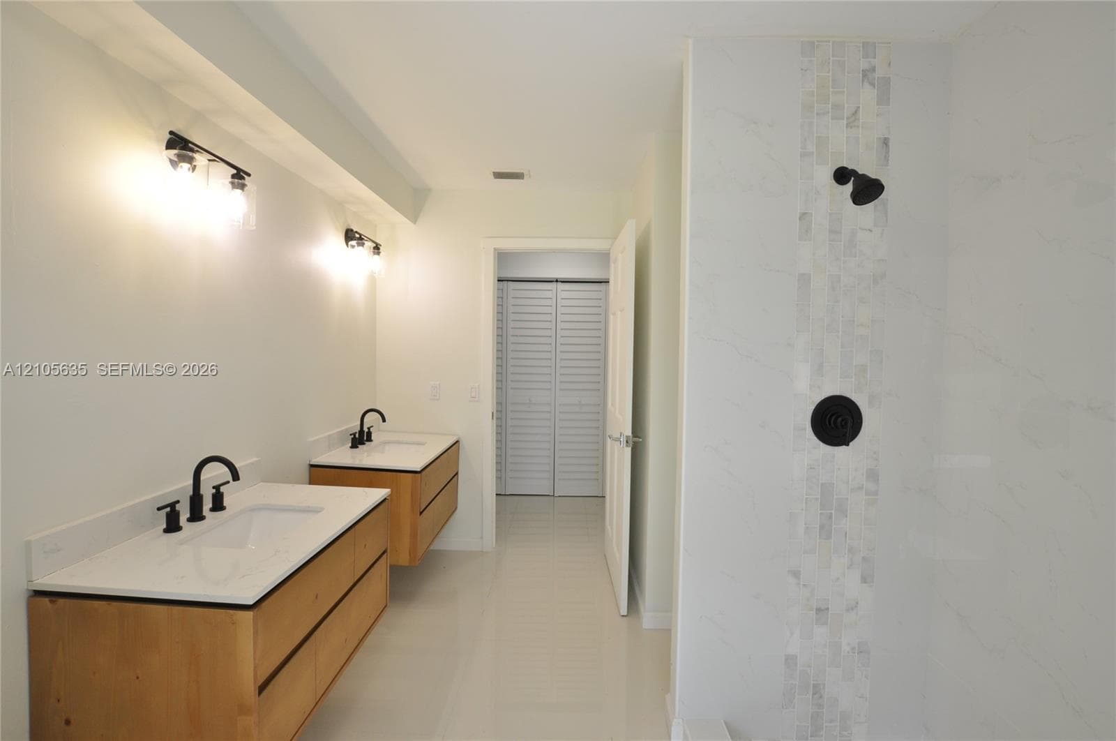 Dual floating wood-finish vanities with rectangular integrated sinks, white quartz countertops, matte black plumbing fixtures, and a glass-enclosed shower featuring a vertical mosaic stone inlay