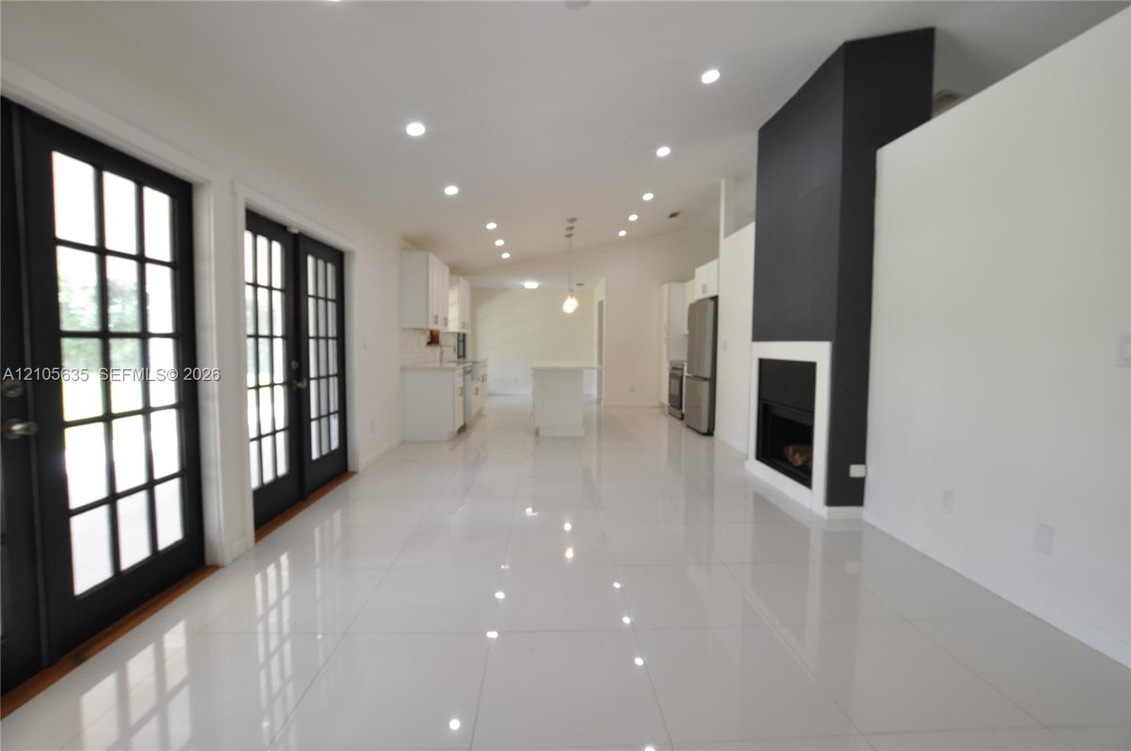 Open interior featuring white tile flooring, recessed lighting, double French doors with black frames, and a floor-to-ceiling fireplace with a contrast hearth