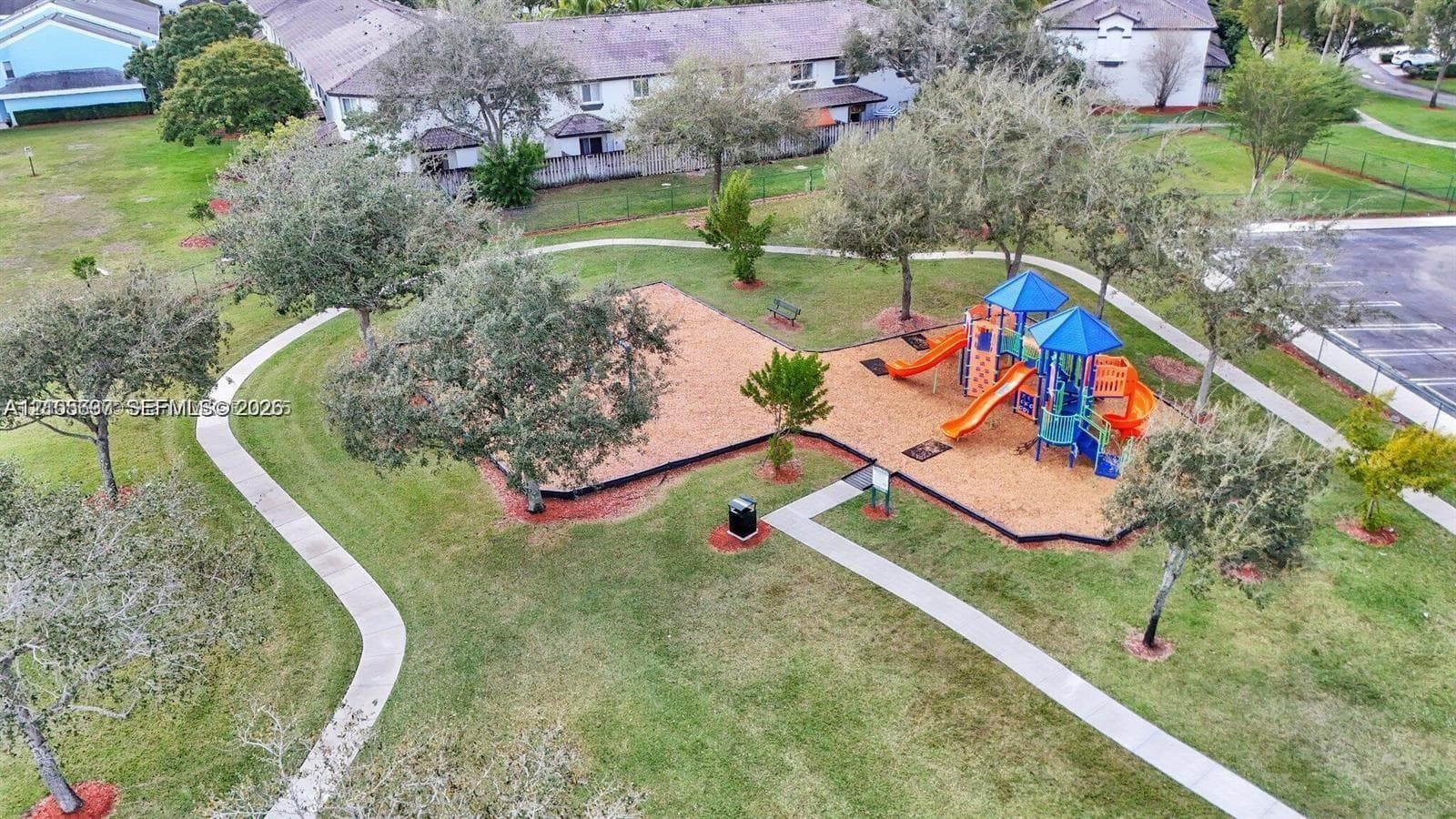 Community recreational area featuring a playground with slides, paved walking paths, mature trees, and landscaped green space