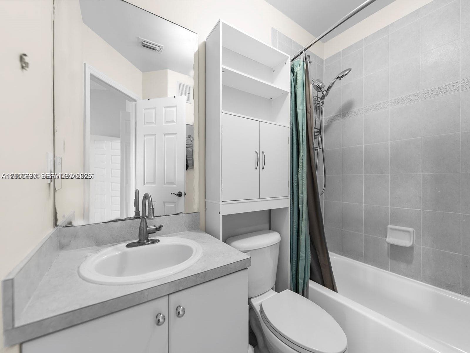 Bathroom featuring a vanity with a solid-surface countertop, an oval under-mount sink, integrated tall cabinet storage, and a tiled shower-tub combination with a handheld shower fixture