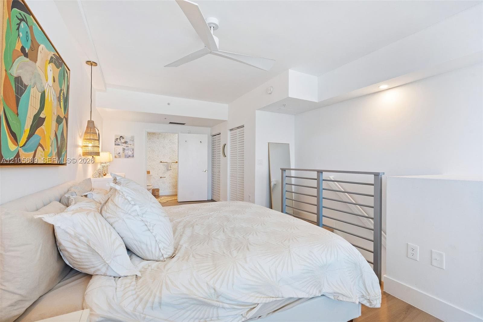 White-painted interior featuring a three-blade ceiling fan, metal horizontal-bar railing, louvered-style closet doors, and wood-finish flooring