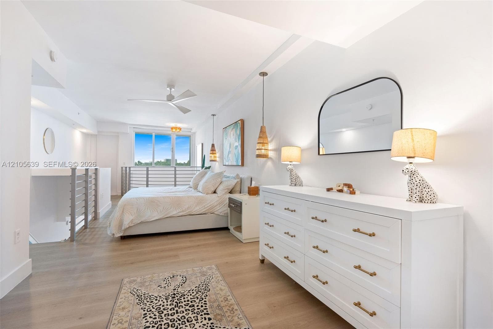 Wood-finish flooring, recessed ceiling lighting, three-blade ceiling fan, arched wall-mounted mirror, and metal railing partition