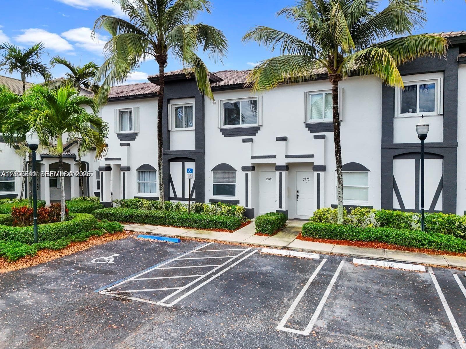 Stucco exterior featuring contrasting dark trim, tile roof, mature palm trees, and manicured shrubbery