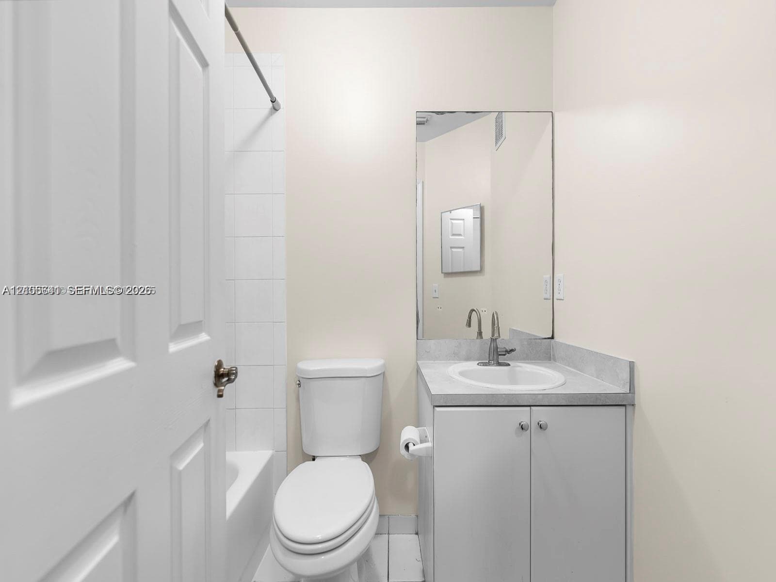 Bathroom featuring a vanity with a solid-surface countertop, an integrated sink, a wall-mounted mirror, a tub-shower combination with white tile surround, and a low-flow toilet