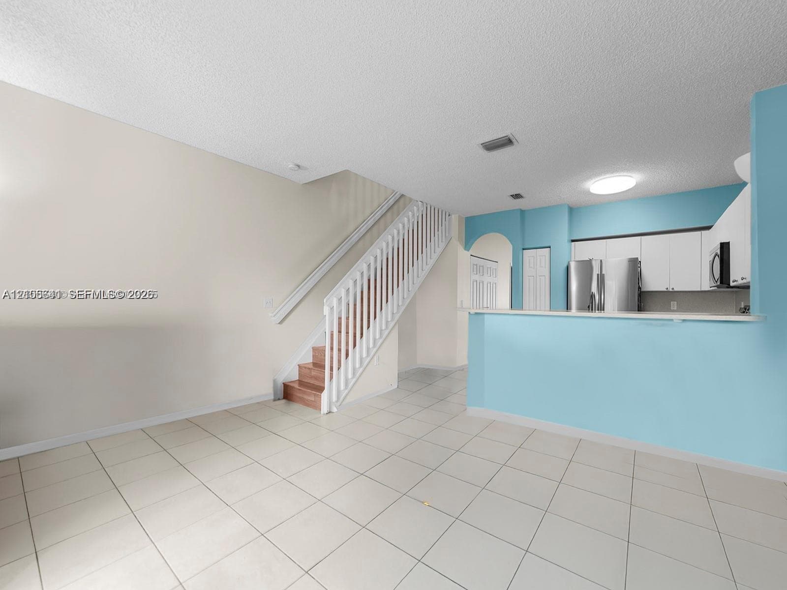 Open-concept floor plan with tile flooring, white cabinetry, built-in breakfast bar, and staircase featuring a painted wood balustrade