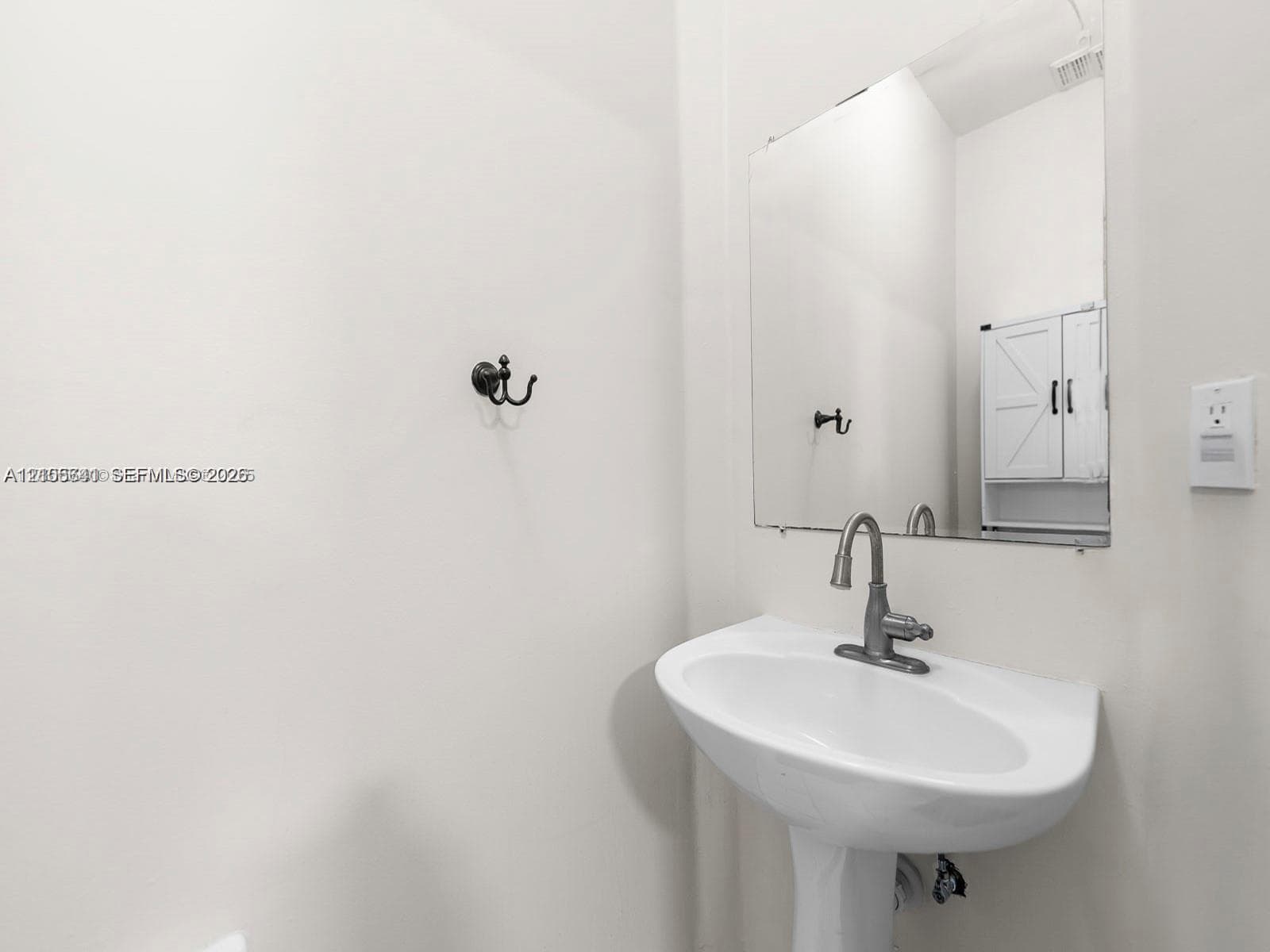 White pedestal sink with a metallic high-arc faucet, wall-mounted mirror, and decorative wall-mounted hardware