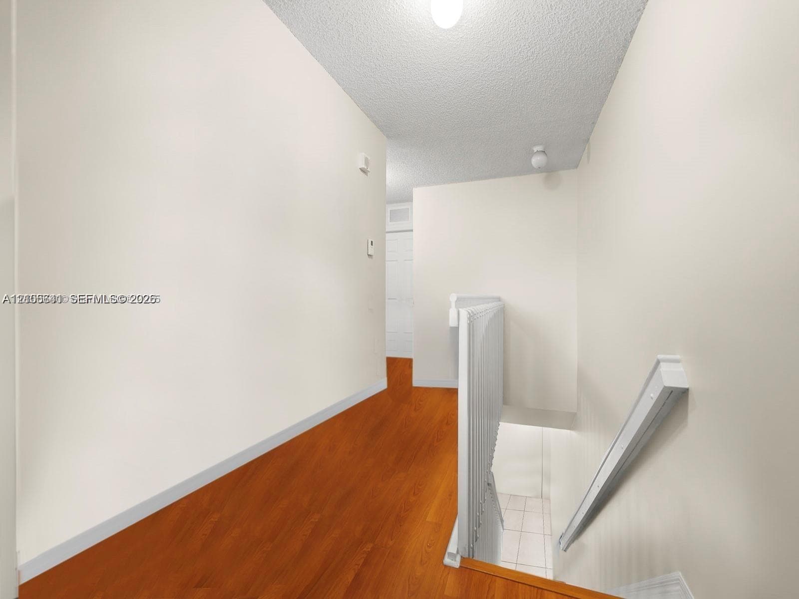 Hallway featuring wood-finish flooring, white walls, textured ceiling, and a white stair railing